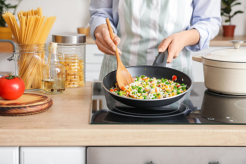 Woman,Cooking,Tasty,Rice,With,Vegetables,On,Stove,In,Kitchen,